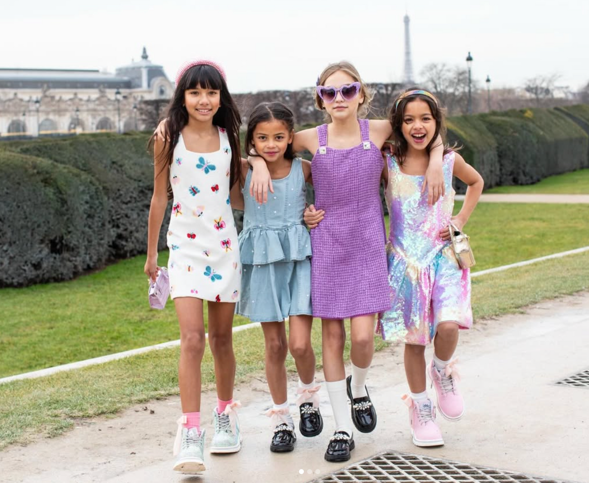 Four young girls posing together outdoors in a park-like setting.